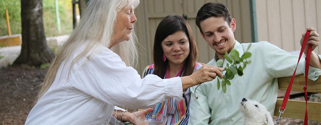 Sr. Martha Ann sprinkles a puppy with holy water as the dog's owners smile