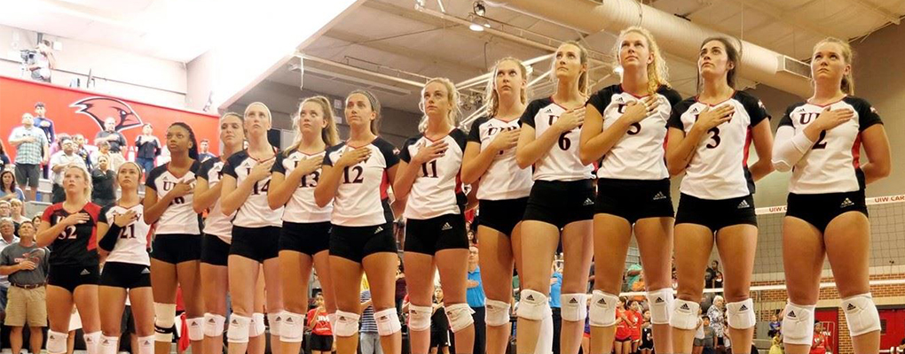 UIW volleyball players stand in a line with their hands over their hearts for the national anthem