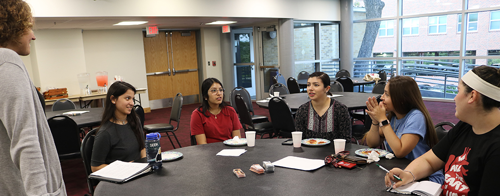 Students sit at a table and look up at the presenter