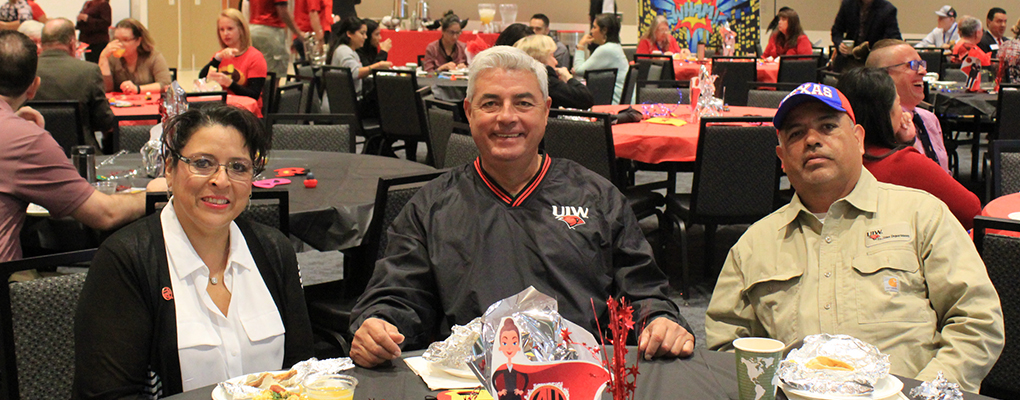 Three UIW employees sit at table and smile at the camera