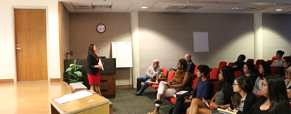 Students sit in auditorium seats and listen as Emma Cantu stands at the front of the room and delivers her presentation