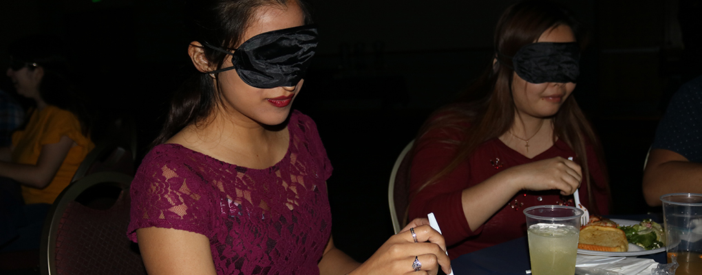 Two girls eat a meal while wearing blindfolds