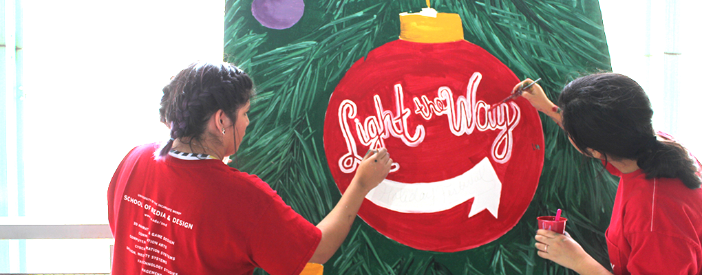 Two girls paint a wooden board in a Christmas theme