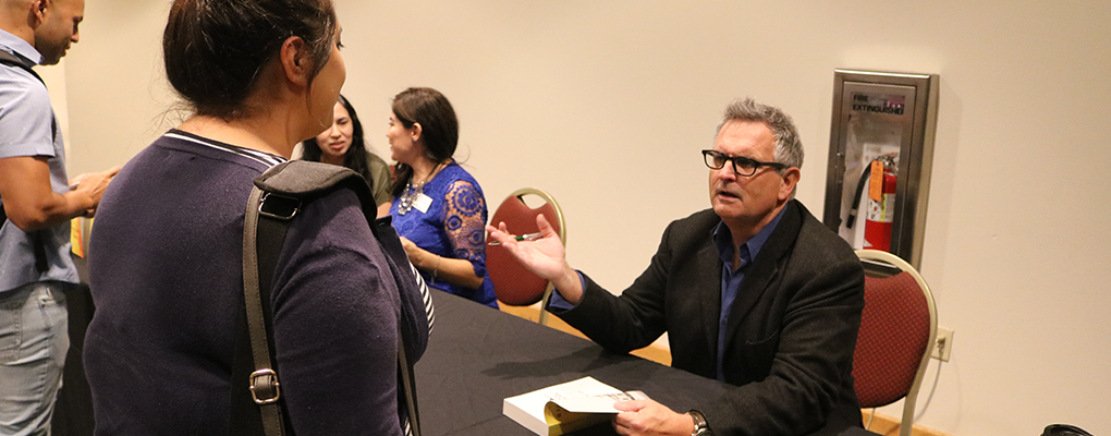 Gilbert King sits at a table and speaks to a woman standing to meet him