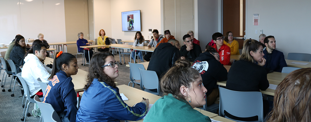 Students sit in a conference room and look at the event speaker