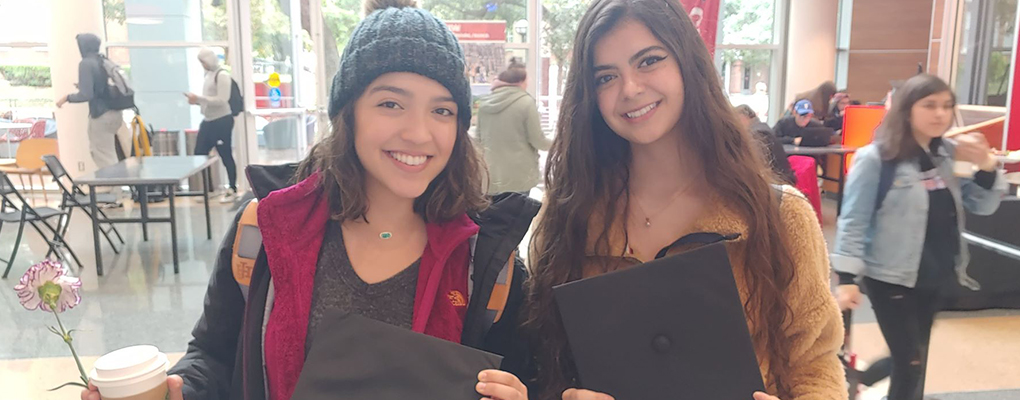 Two students smile and hold their graduation caps 