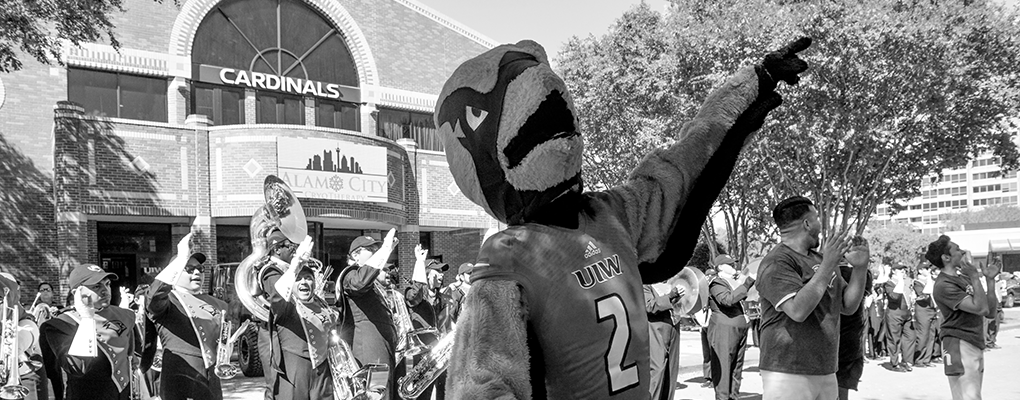 Red the Cardinal stands in front of the marching band and waves to the crowd