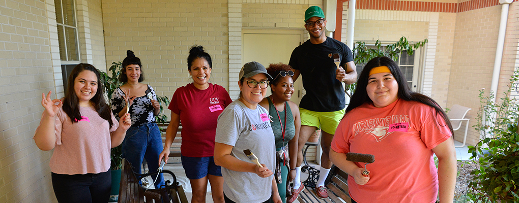 Volunteers look at the camera smiling while holding tools like paint brushes