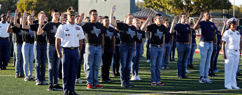 Military enlistees stand on the football field with their right arms raised