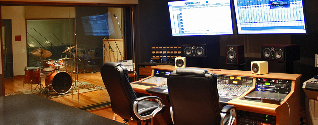 An image of UIW's recording studio with sound boards and TV screens, a drum set and audio speakers