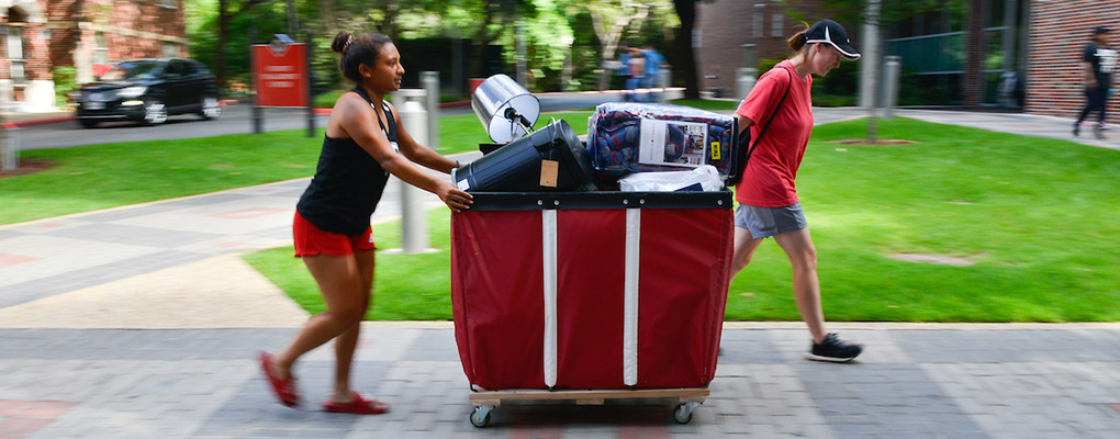 UIW volunteers move a large red bin with luggage to the dorm area