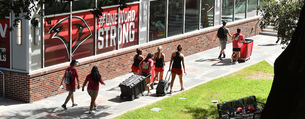 Students push red bins with luggage across campus