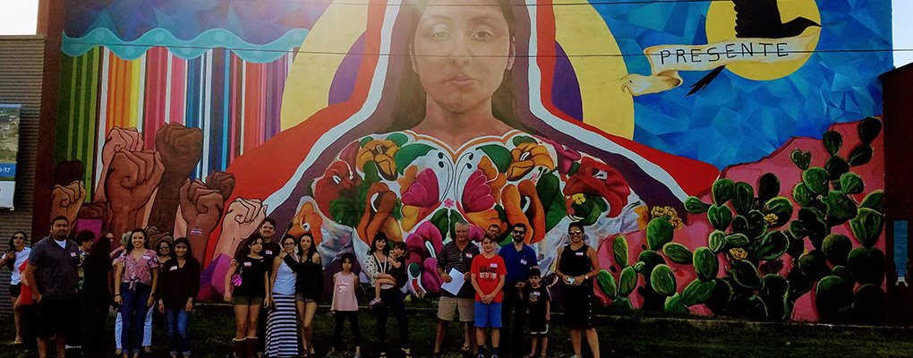 UIW community members pose in front of a large painted mural of a 20-year-old indigenous woman from Quetzaltenango, Guatemala