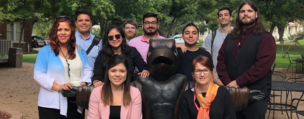 More UIW employees pose for a photo around a bench in the shape of a Cardinal