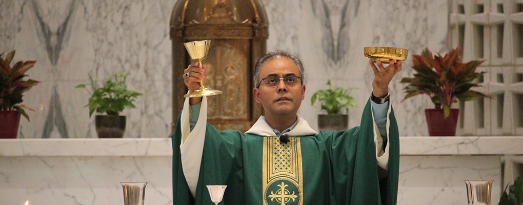 A priest stands behind the altar and holds up communion 