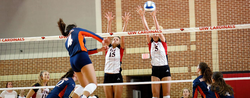 UIW women's volleyball players jump and reach for the ball as it comes over the net
