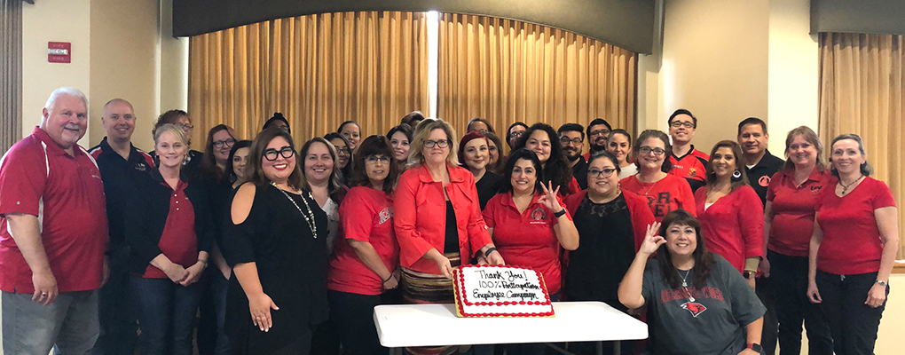 A group of people gathers around a cake and smiles at the camera