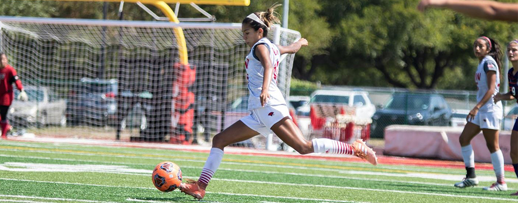 A women's soccer player runs down the field while kicking a soccer ball