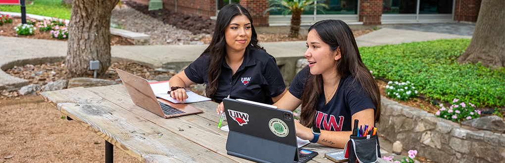 Students smiling whilee sitting on a bench outside of the library