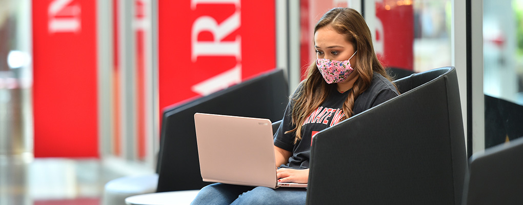 Student working on laptop in the student engagement center while wearing a mask