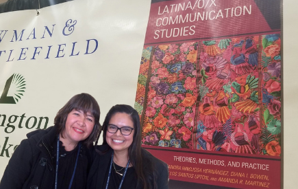 Two women posing in front of poster