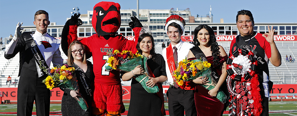 The 2019 UIW Homecoming court and Red the Cardinal stand on the football field