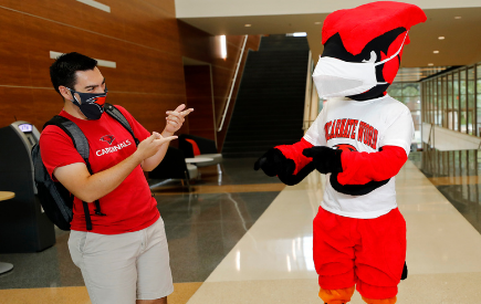 A student interacts with Red the Cardinal mascot