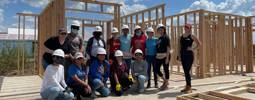 Students pose in front of a house under construction