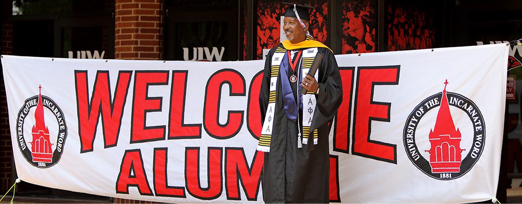 Graduate standing in front of an alumni banner