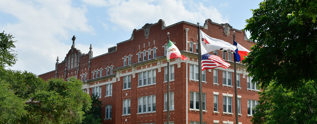 Flags wave in front of a red brick building 