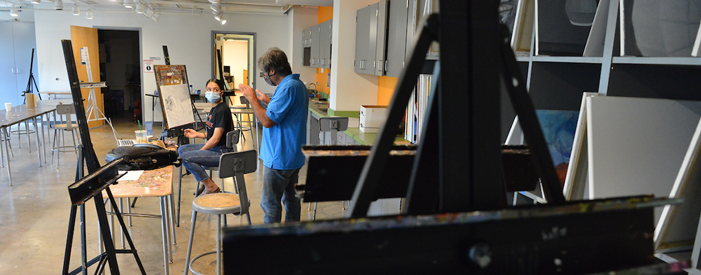 An instructor and art student converse near an easel