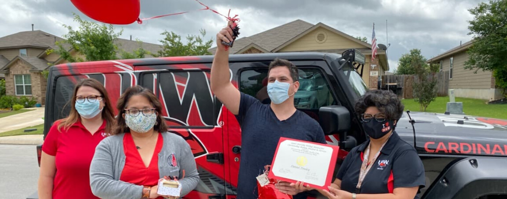 A group of people stand in front of the UIW Jeep, holding certificates and balloons