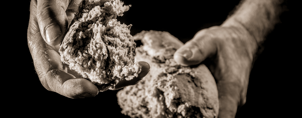 a piece of bread is broken in half and extended by hand