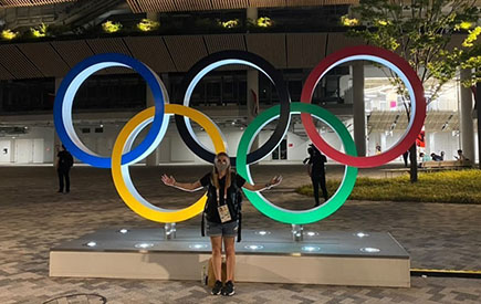A woman stands in front of Olympic rings