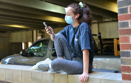 A student wearing a mask looks at her phone