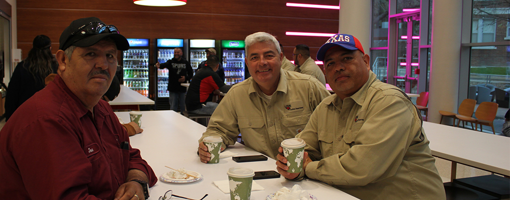 Three UIW employees sit at a table with coffee and look at the camera