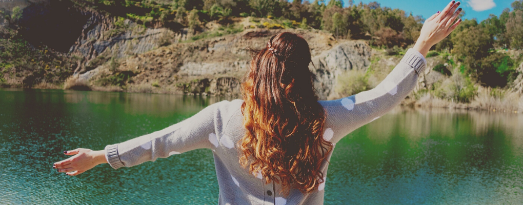 A woman overlooks the water with her hands in the air