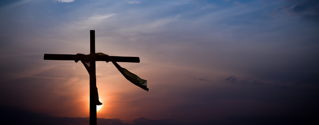 The silhouette of a cross against an evening sky