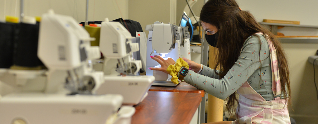 A student wearing a mask works with a sewing machine