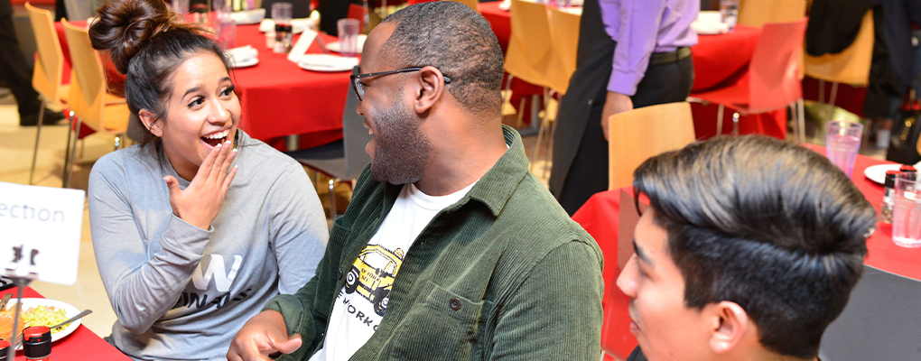 Three students have a conversation seated at a table