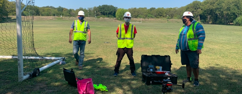 Three UIW students in yellow vests and hard hats stand outdoors
