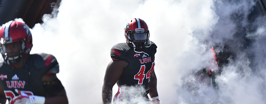 A UIW football player runs onto the field surrounded by white smoke