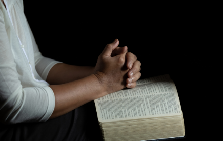Hands folded in prayer over a Bible