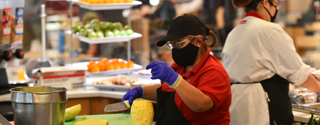 A staff member works in the dining hall, slicing fruit