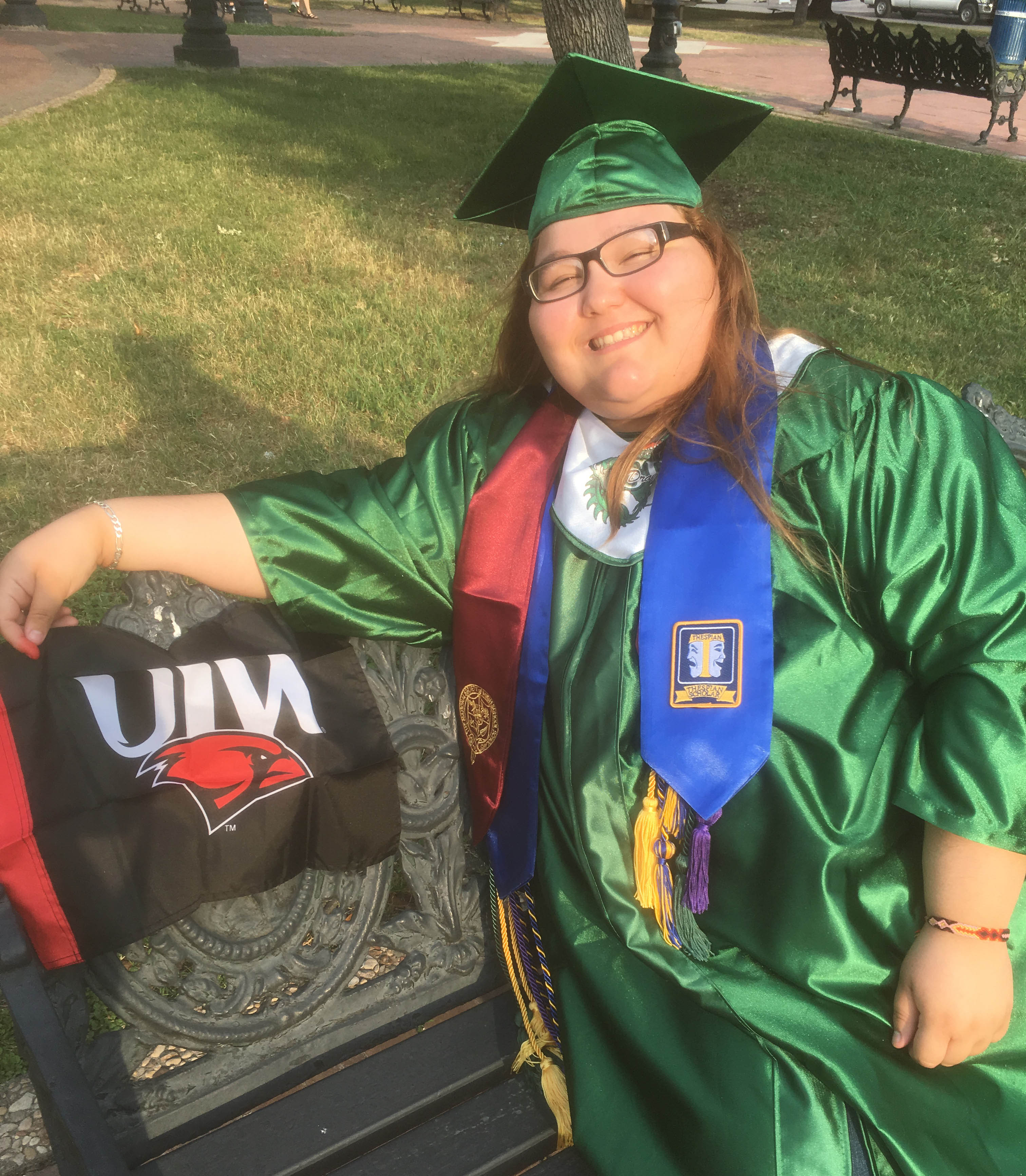 A student poses for a photo in a cap and gown next to a UIW flag