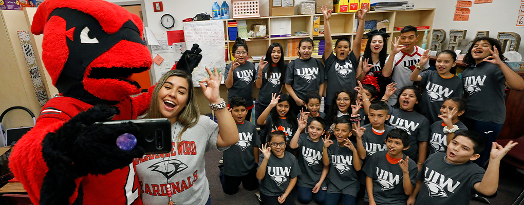 Red the Cardinal takes a selfie with a classroom full of students in UIW t-shirts