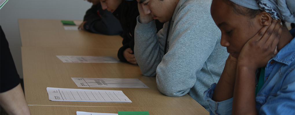 People sit at desks and look down at a sheet of paper