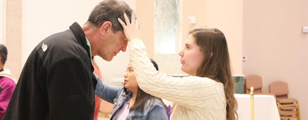 A student blesses a man with ashes in a church 