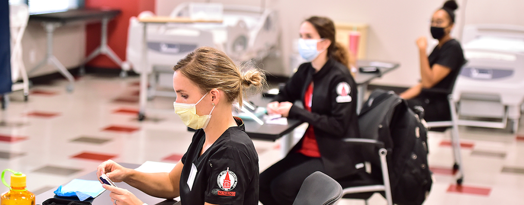 Nursing students wearing masks sit at desks and work