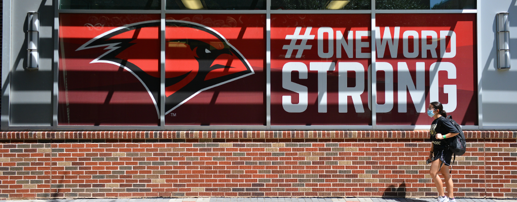 A student walks in front of a sign that says "One Word Strong."